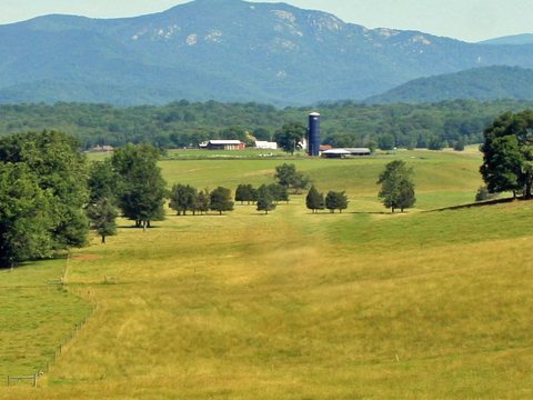 Rocky mountain peak above green farm fields with a blue silo